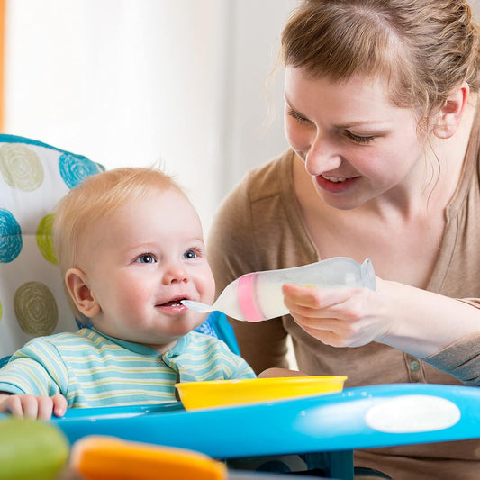 Mother feeding baby with squeeze bottle and soft silicone spoon
